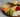 Cheese board with sliced cheese, green grapes, raspberries, tangerine slices, walnuts, and bread on wooden platter